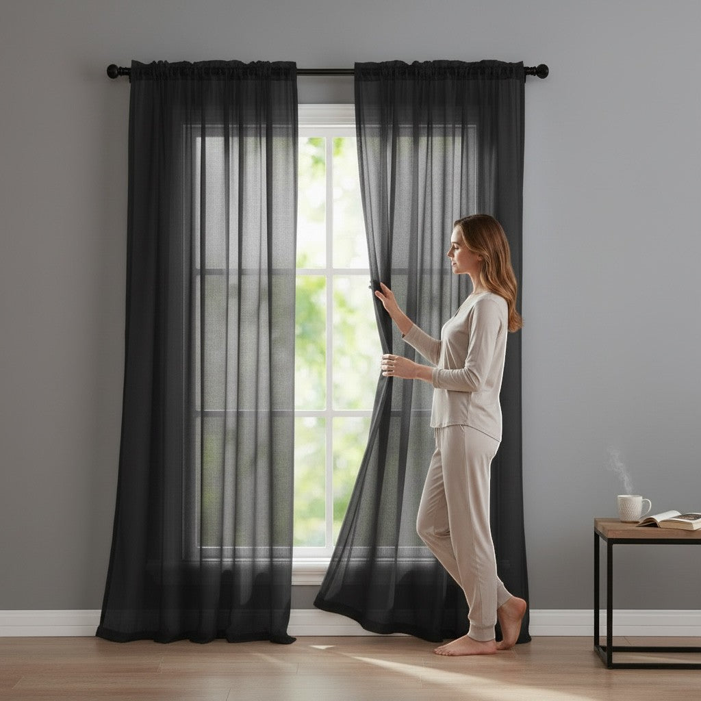Home Appeal sheer black window curtain panels hanging on a rod with a woman standing beside them in a modern room